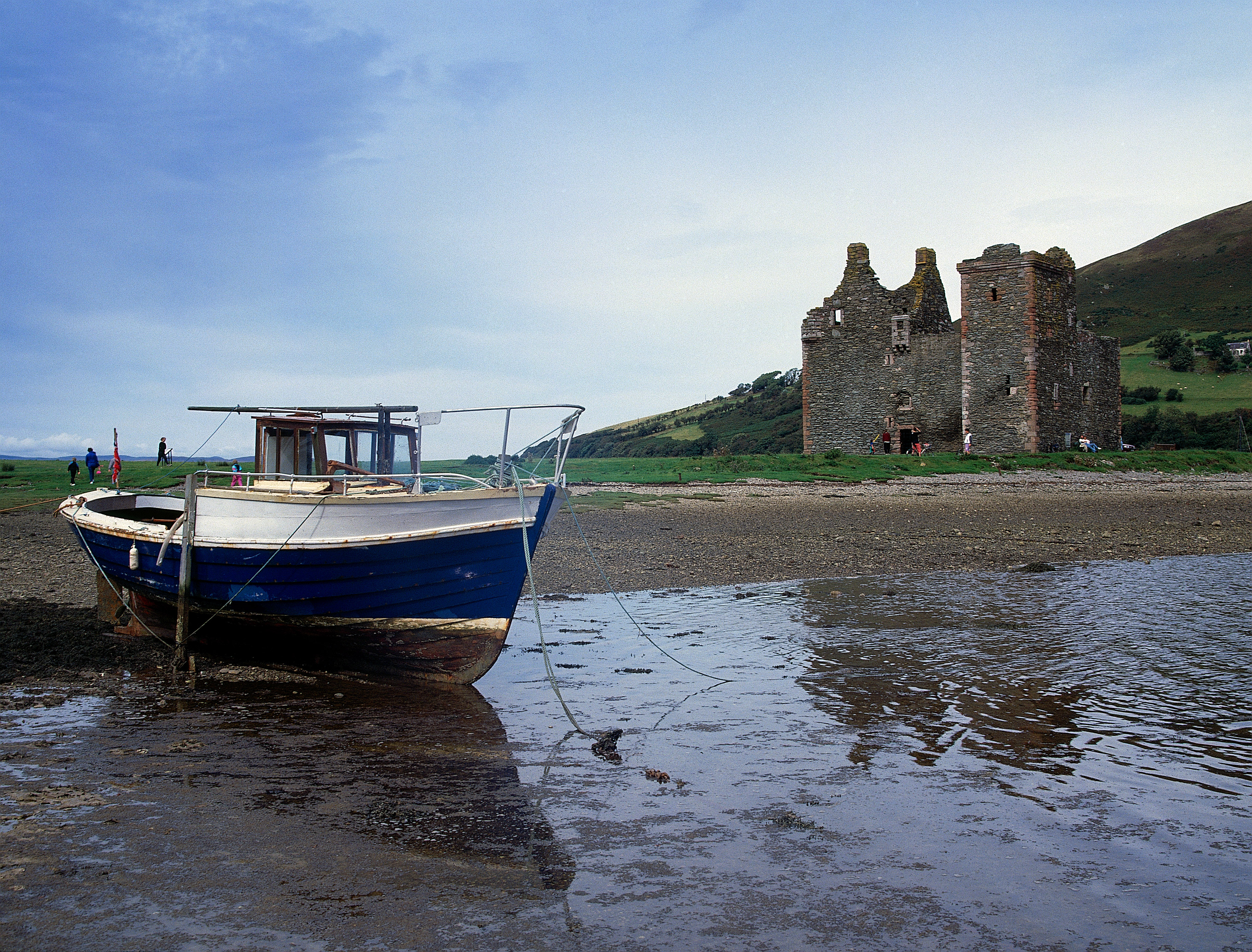 A fishing boat at low tide in front of the ruins of Lochranza Castle.