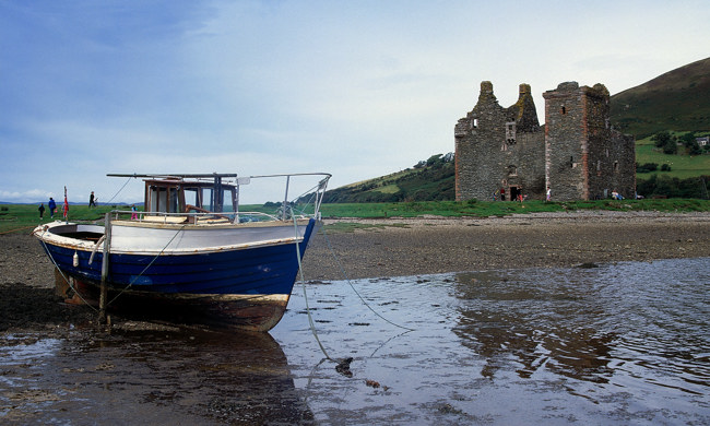 A fishing boat at low tide in front of the ruins of Lochranza Castle.