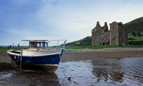 A fishing boat at low tide in front of the ruins of Lochranza Castle.