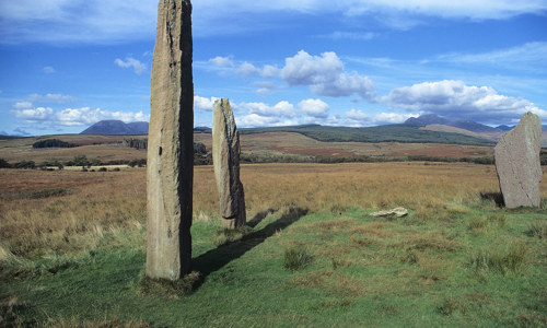 Three large standing stones in a marshy landscape