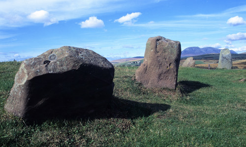 A large boulder and several low standing stones in a field.