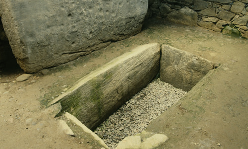 A grave like hole inlaid with stone slates inside a stone cairn.
