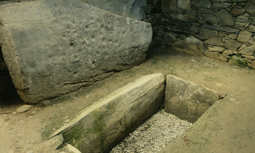 A grave like hole inlaid with stone slates inside a stone cairn.