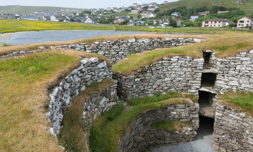 The impressively intact remains of the broch are several storeys high. The stone walls are grass covered.