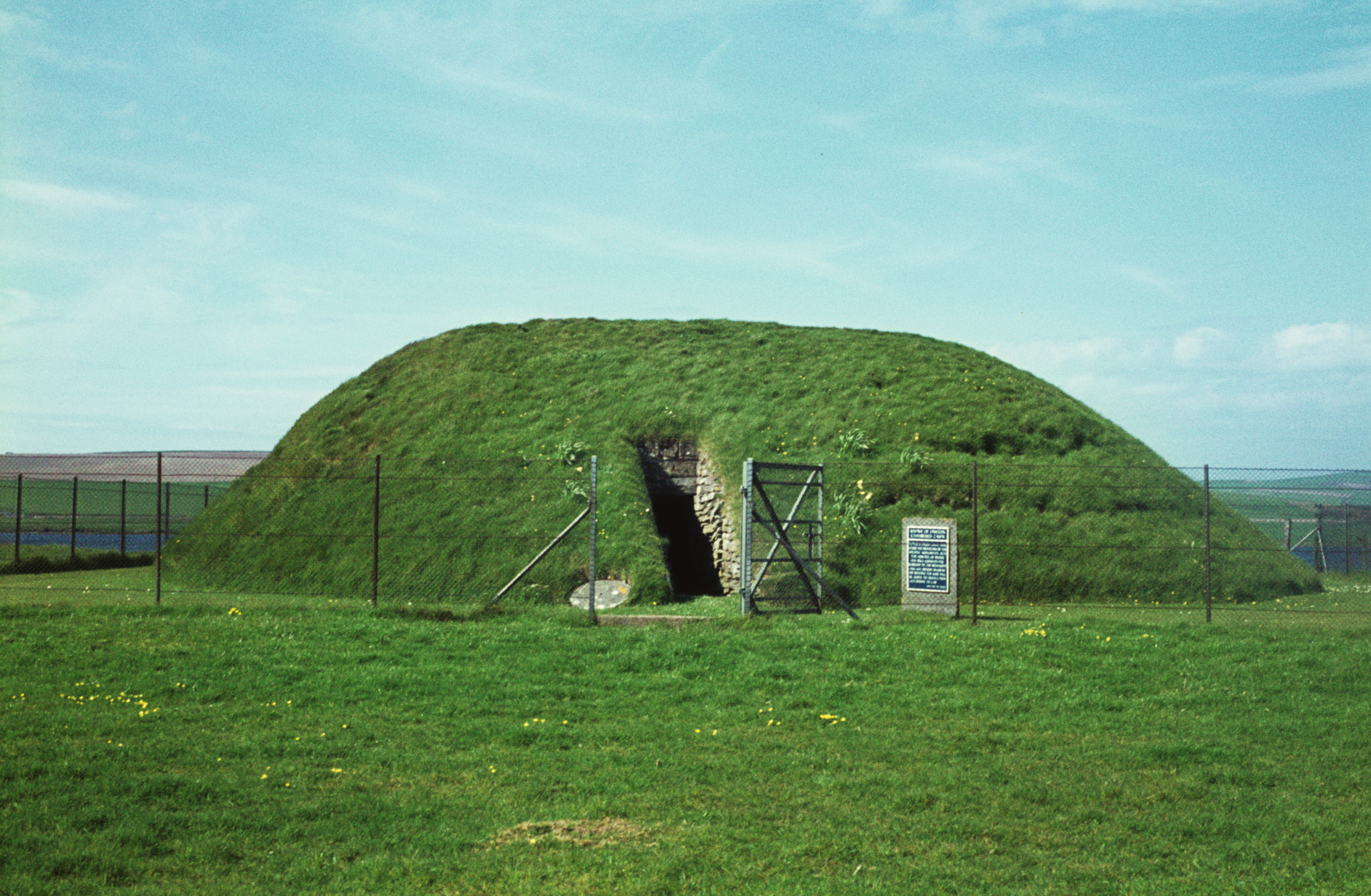 A grassy cairn with an open entrance, surrounded by a fence