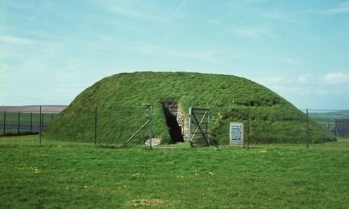 A grassy cairn with an open entrance, surrounded by a fence