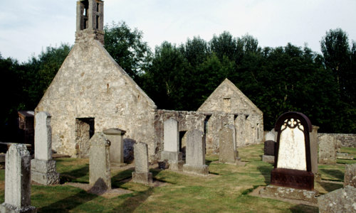A few gravestones stand in front of a roofless church with a bell tower.