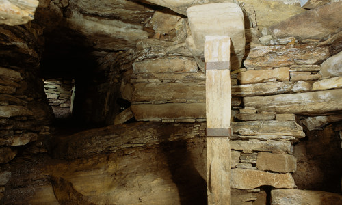 The interior of Rennibister earth house. The stone ceiling is held up by a wooden beam.