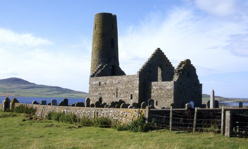 The complete but roofless ruin of St Magnus Church with a large round tower just behind it