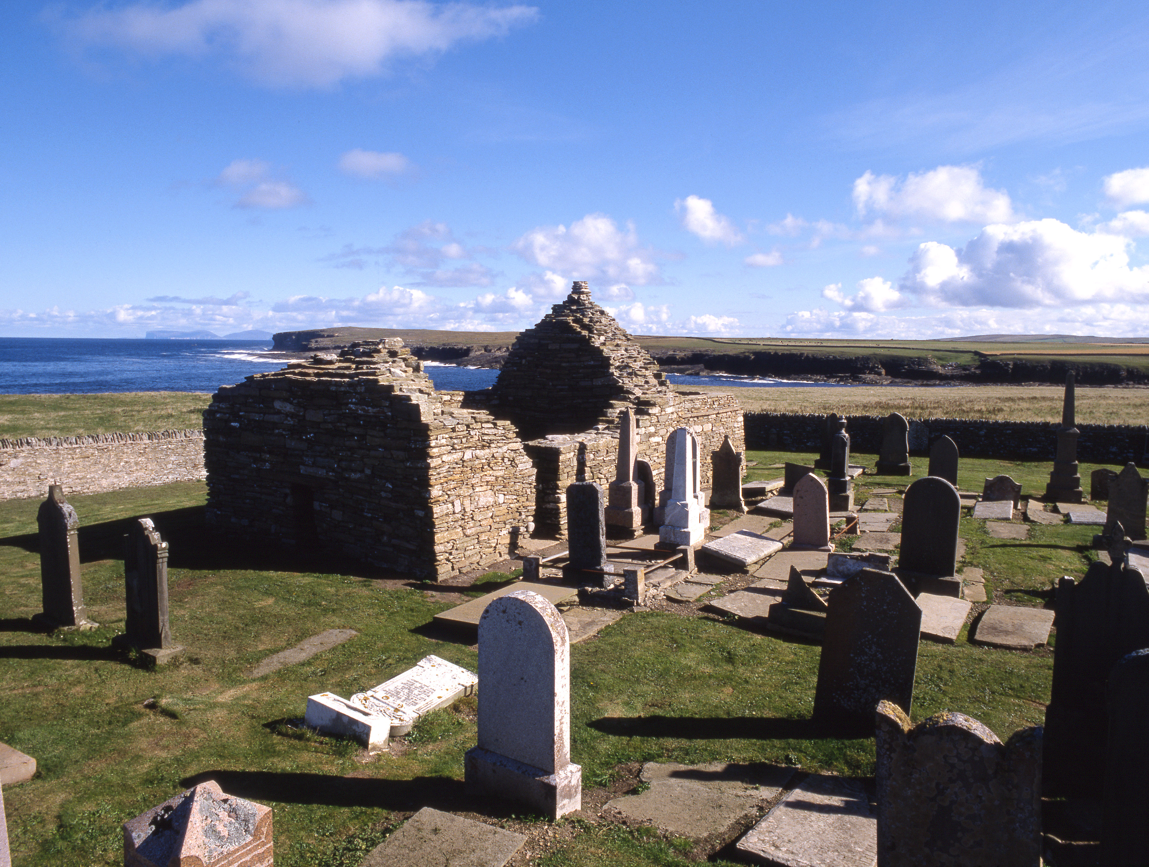 The roofless remains of a chapel by the sea, surrounded by a small graveyard
