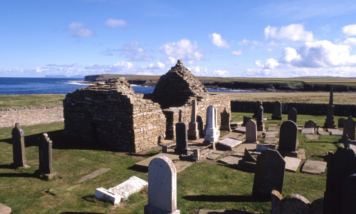 The roofless remains of a chapel by the sea, surrounded by a small graveyard