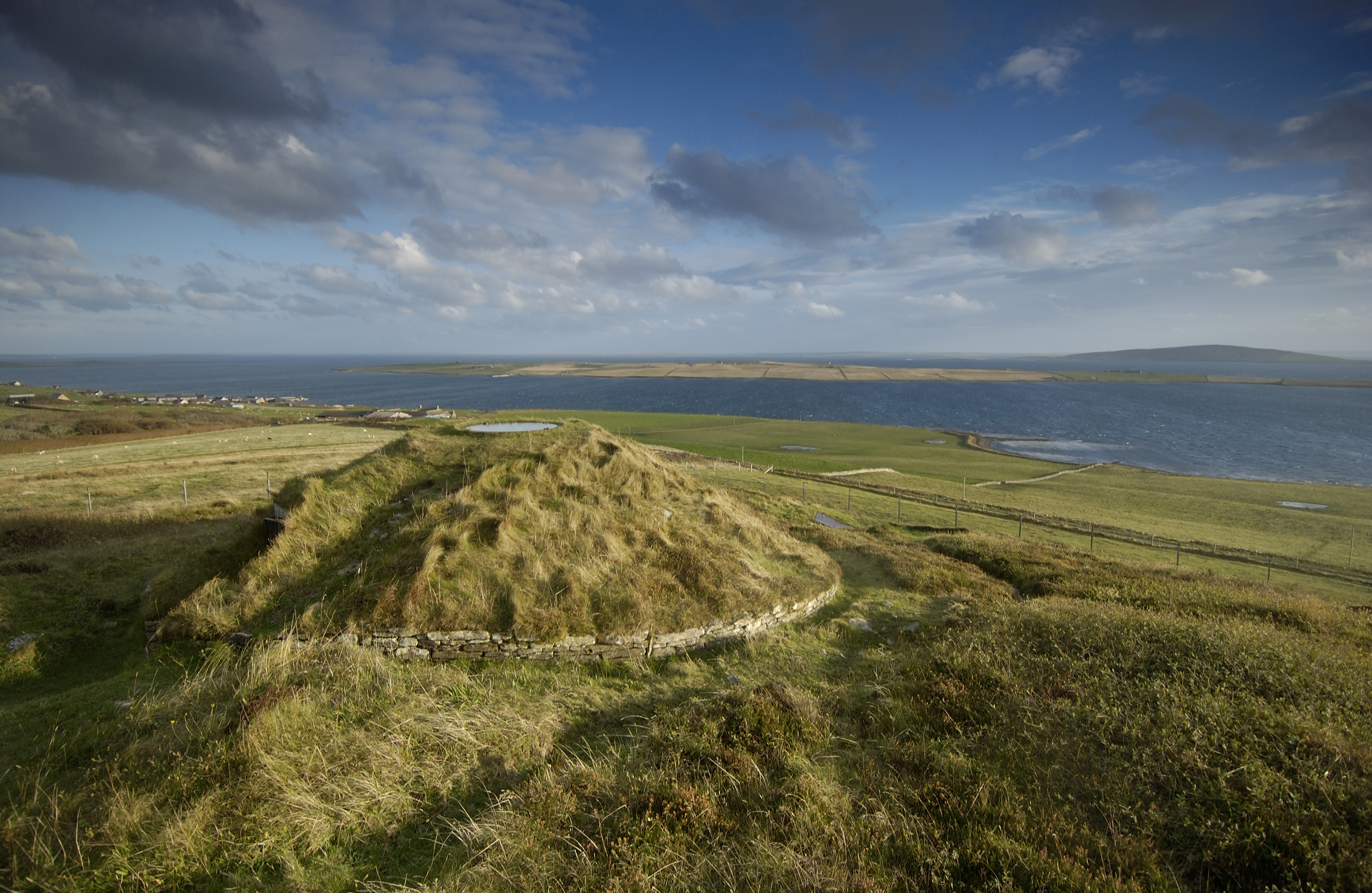 A grass-covered burial cairn on a field close to the sea