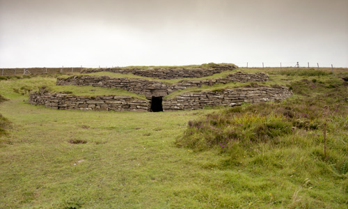 A three layered stone cairn, covered by grass