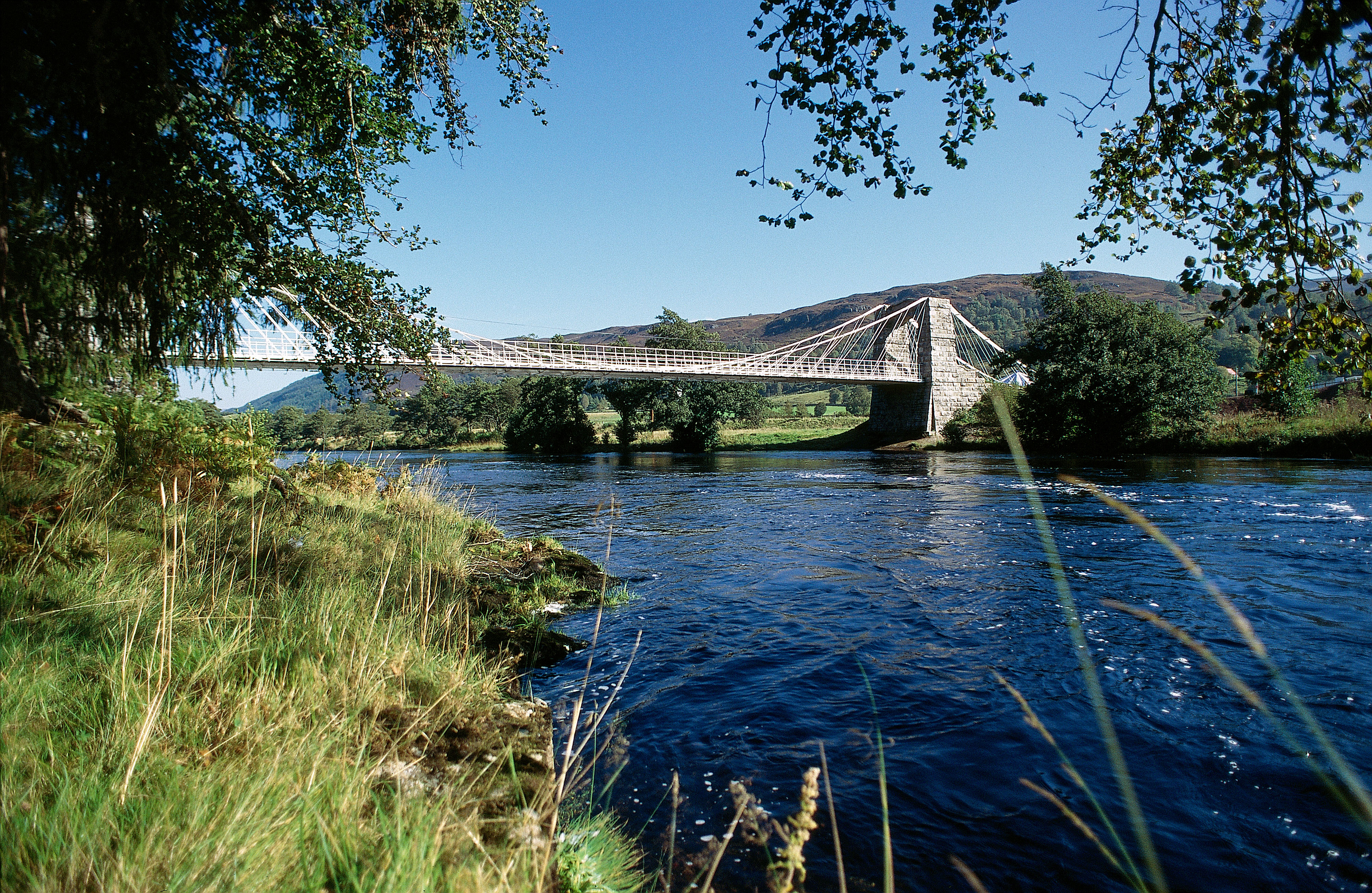 A white and grey suspension bridge spanning the river Oich.