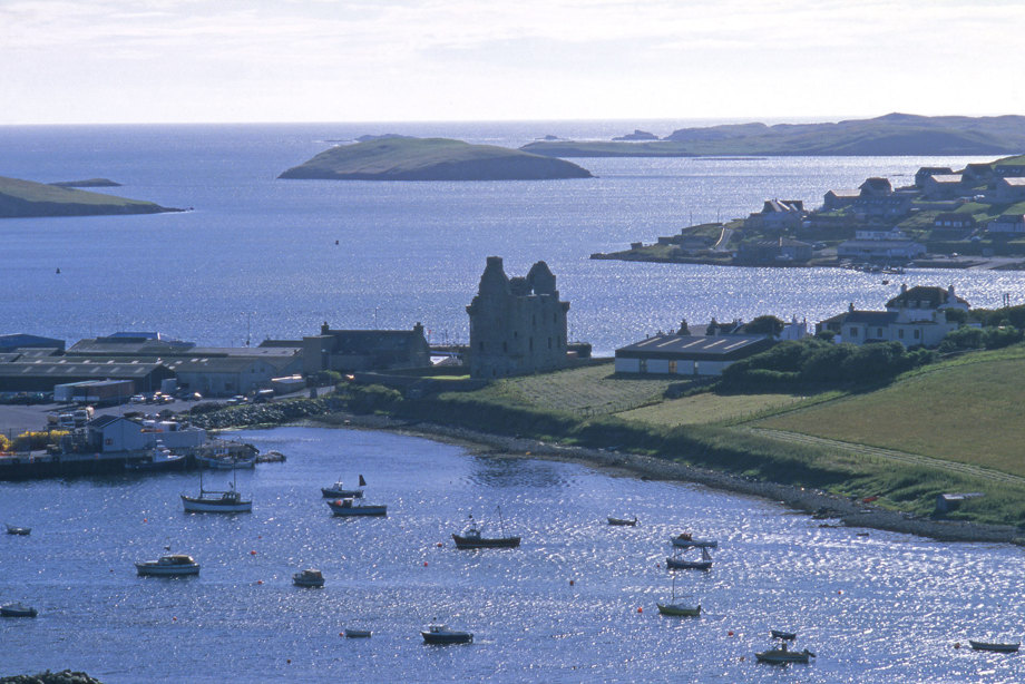 Scalloway Castle seen from a distance. It sits on a small landmass between a harbour and the sea