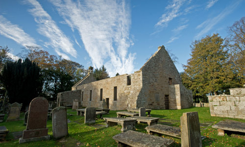 A small roofless church surrounded by trees and gravestones
