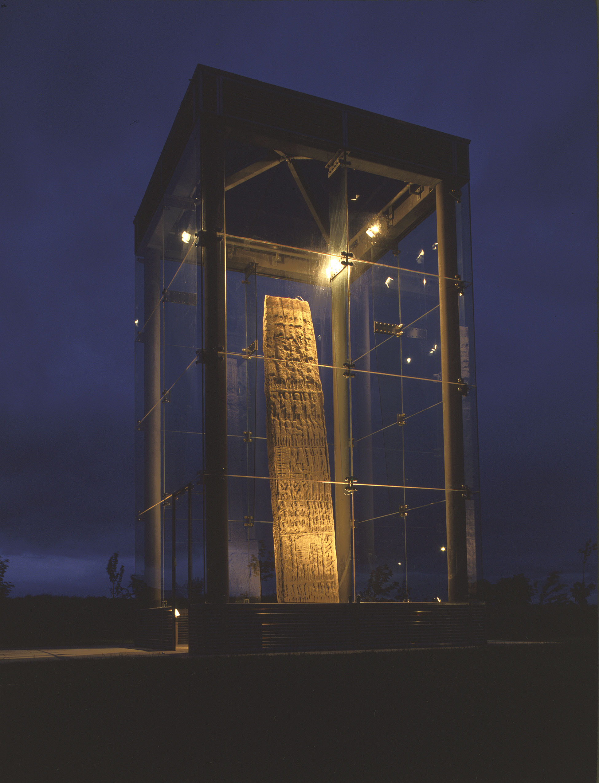 A very tall standing stone is encased by a glas enclosure and is lit up during the night