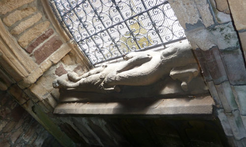 A tomb with a carved man on top by a window at Beauly Priory