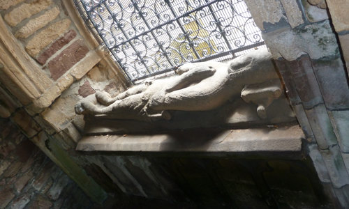 A tomb with a carved man on top by a window at Beauly Priory