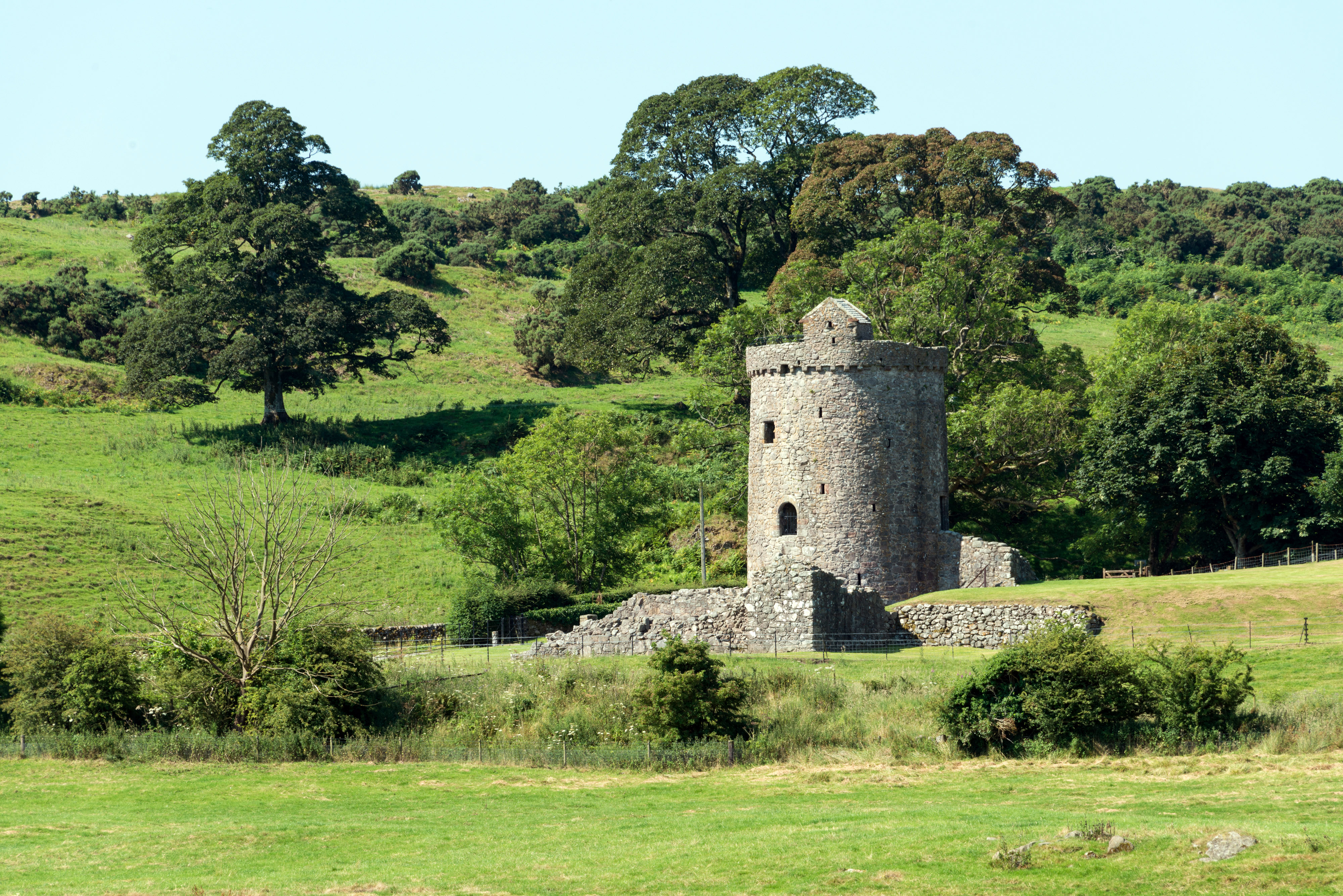 A round stone tower with the foundation of walls on a hilly green landscape