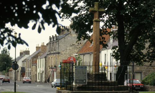 A fine stone cross on a modern base in a calm village road