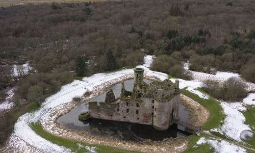 An aerial view of Caerlaverock Castle in winter, showing snow and surrounding woodlands