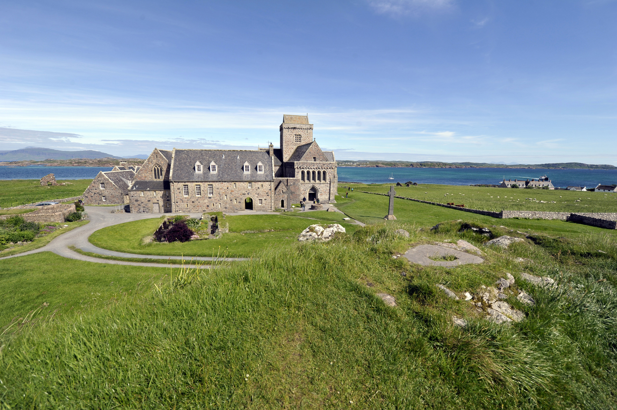 A historic stone abbey with a slate roof, and expansive grassy space around it