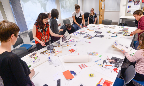 A group of people stand around a large white table covered in photos and paper.