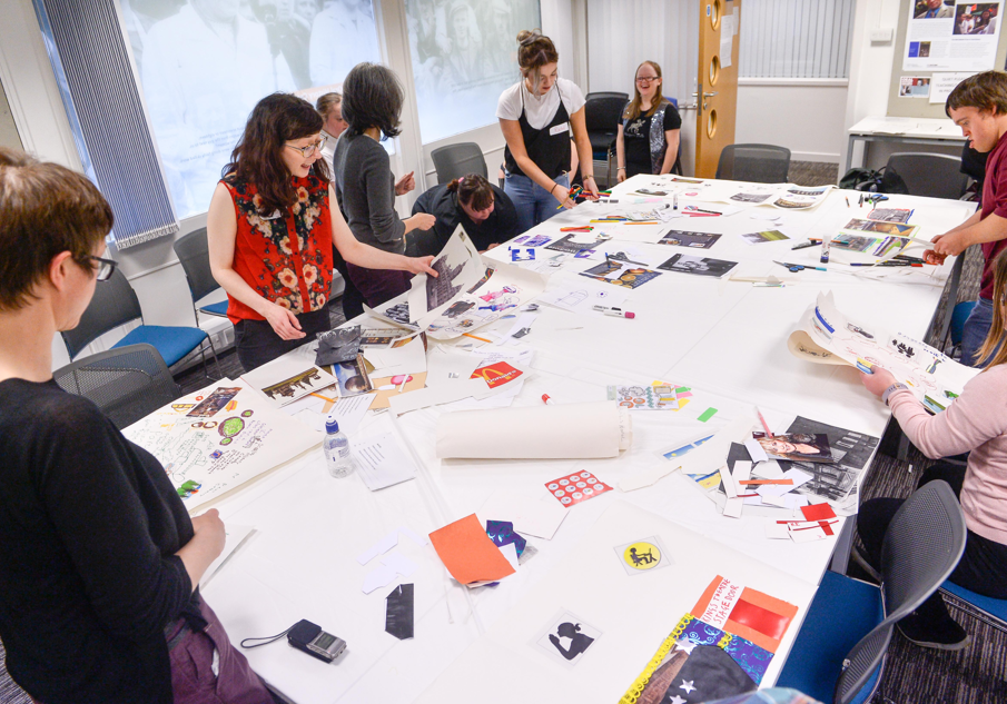 A group of people stand around a large white table covered in photos and paper.