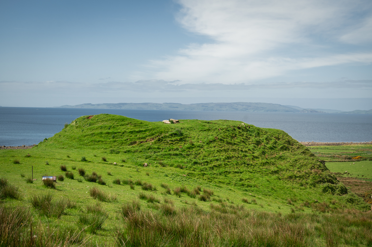 A wide mound with ridge edges, with grass growing on it. There is sea in the distance. 