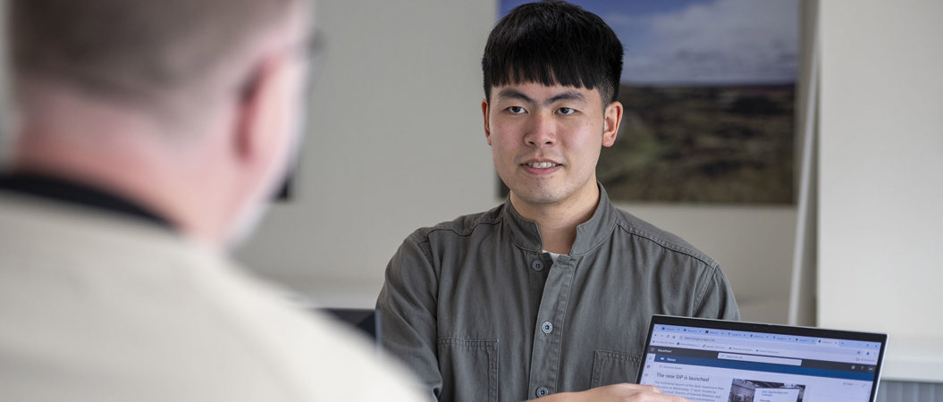 Man in green shirt stand holding a laptop while pointing at the screen