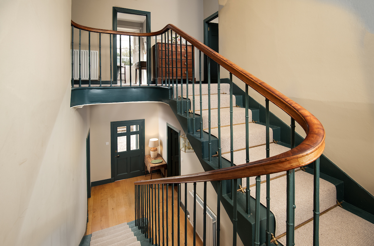 A stairwell featuring a black banister with metal spindles, dark blue painted stairs with a cream carpet runner down the middle