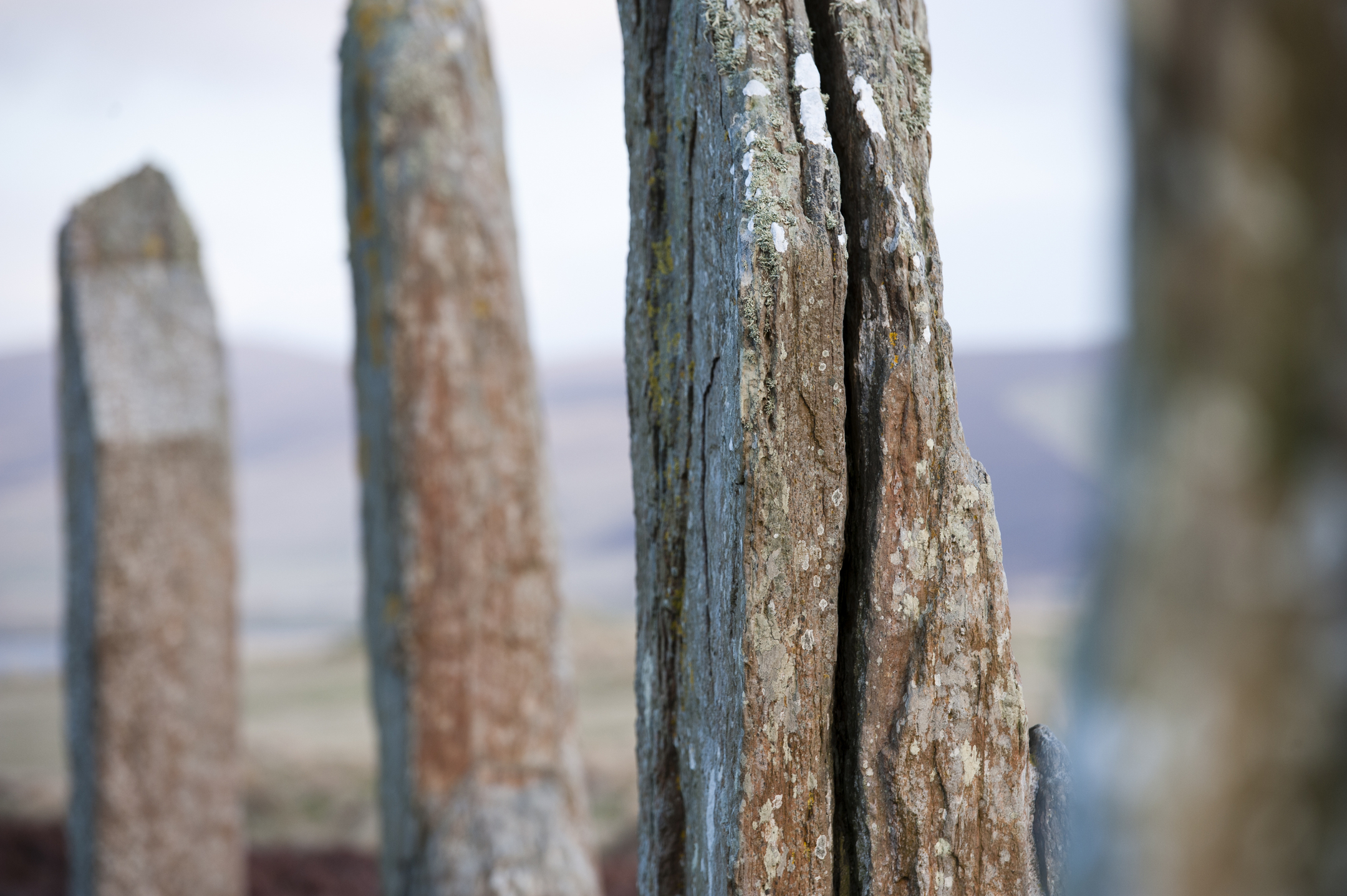 A close-up photo of three ancient standing stones, weathered by age to the point one appears to be splitting in two. 