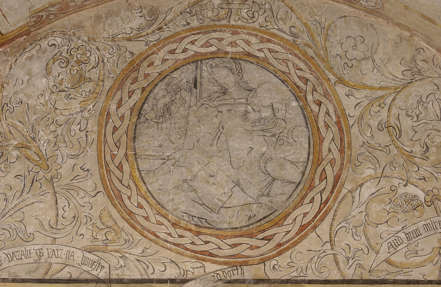 A decorated, painted wall. There is a plaited circle in the centre, with gold and orange colouring. In the centre is a faded outline of a woman. Around the outside there are the outline of flowers. 