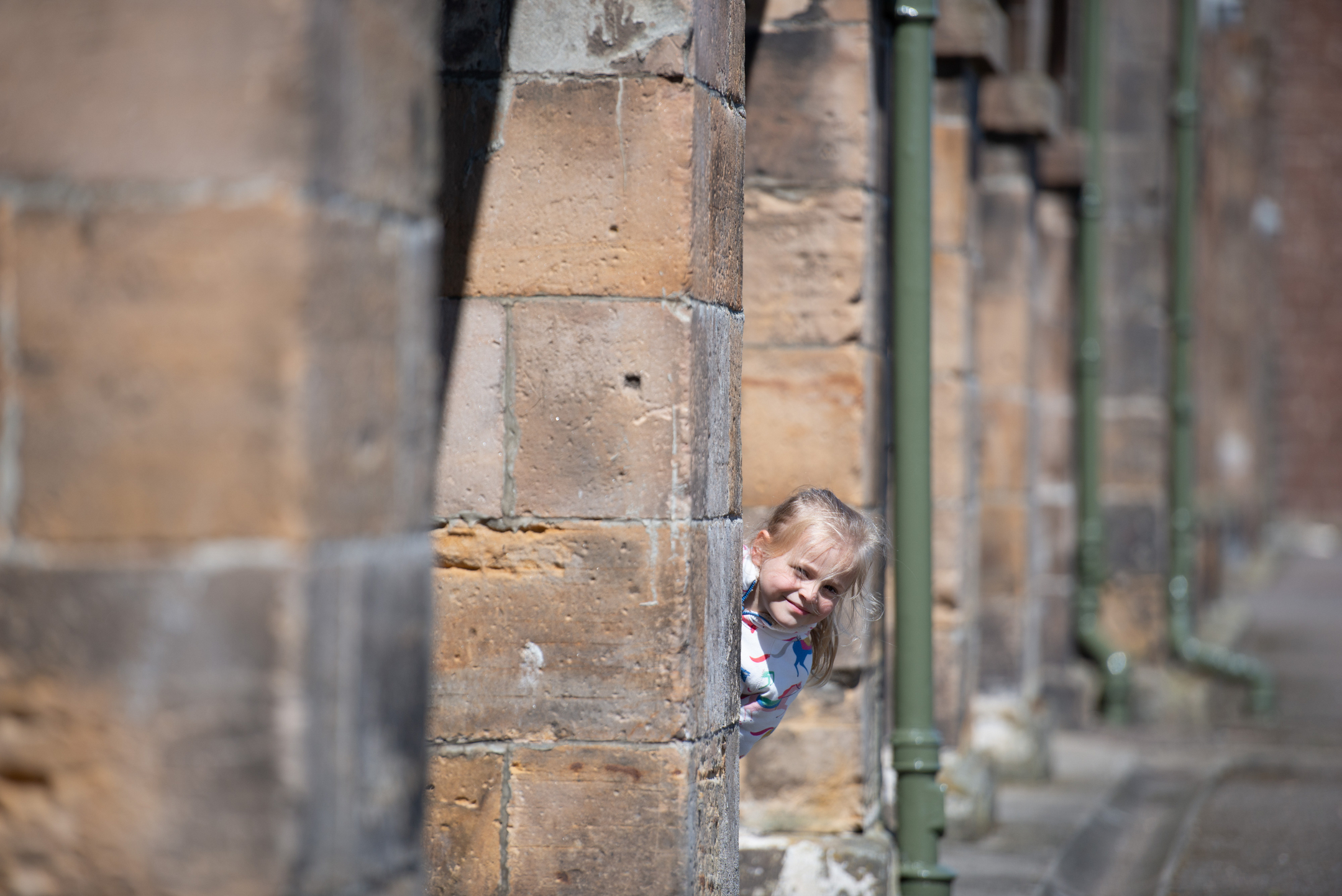 A child playfully peeks out from behind a tall sandstone pillar along the colonnade at Fort George.