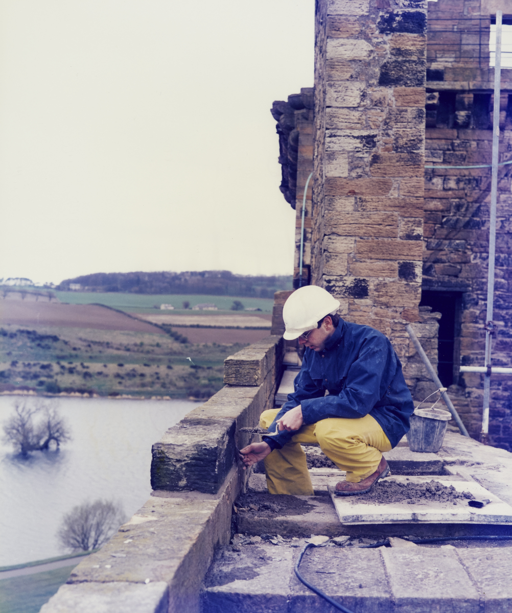A person in a hard hat repairs a wall near the top of the palace