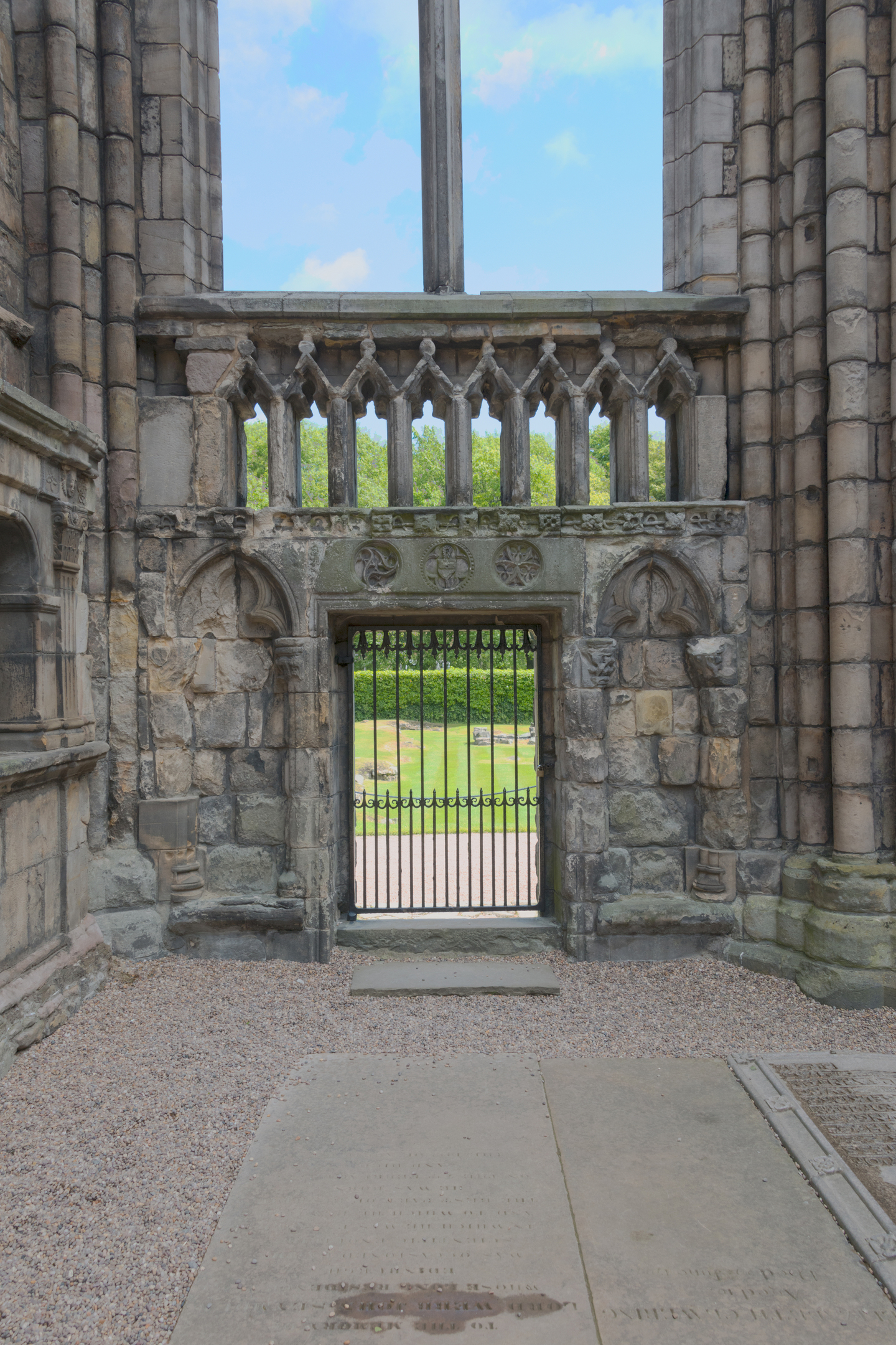 A straight on view of the gated north-east doorway of Holyrood Abbey. The abbey gardens can be seen beyond the iron gate. 