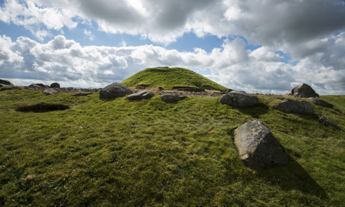 A grass covered dome-shaped tomb, surrounded by a few stone slabs