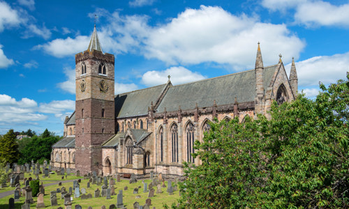 A photograph of a large church with a tower and a big graveyard on a sunny day.