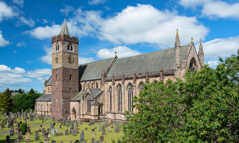 A photograph of a large church with a tower and a big graveyard on a sunny day.
