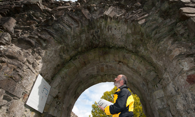 A surveyor under an archway inspecting a sign, wearing a yellow jacket