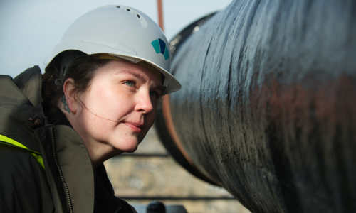 A woman in a hardhat leans in to study the barrel of a massive iron cannon, which is suspended next to her.