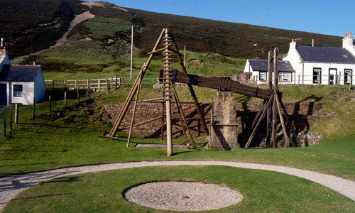 A wooden water balance pump outdoors surrounded by white cottages
