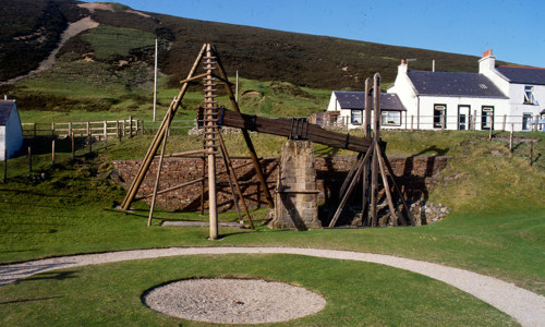 A wooden water balance pump outdoors surrounded by white cottages