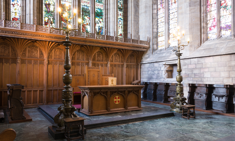 The altar inside Dunblane Cathedral, flanked by candles and surrounded by stained glass windows.