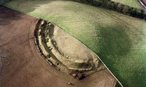 An aerial view of a motte hill, half with earthworks exposed, the other half turfed over.
