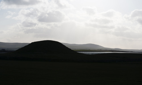 Silhouette of hill in the foreground, with loch and clear view of hills in the background