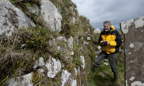 A scheduling staff member undertaking some survey work at the remains of a stone building.