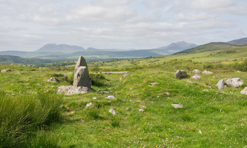 A few stones that belonged to a drystone building on a grassy landscape with hills in the distance