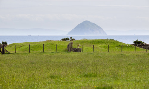 General view of Torrylin neolithic chambered cairn on Arran with Ailsa Craig in the background